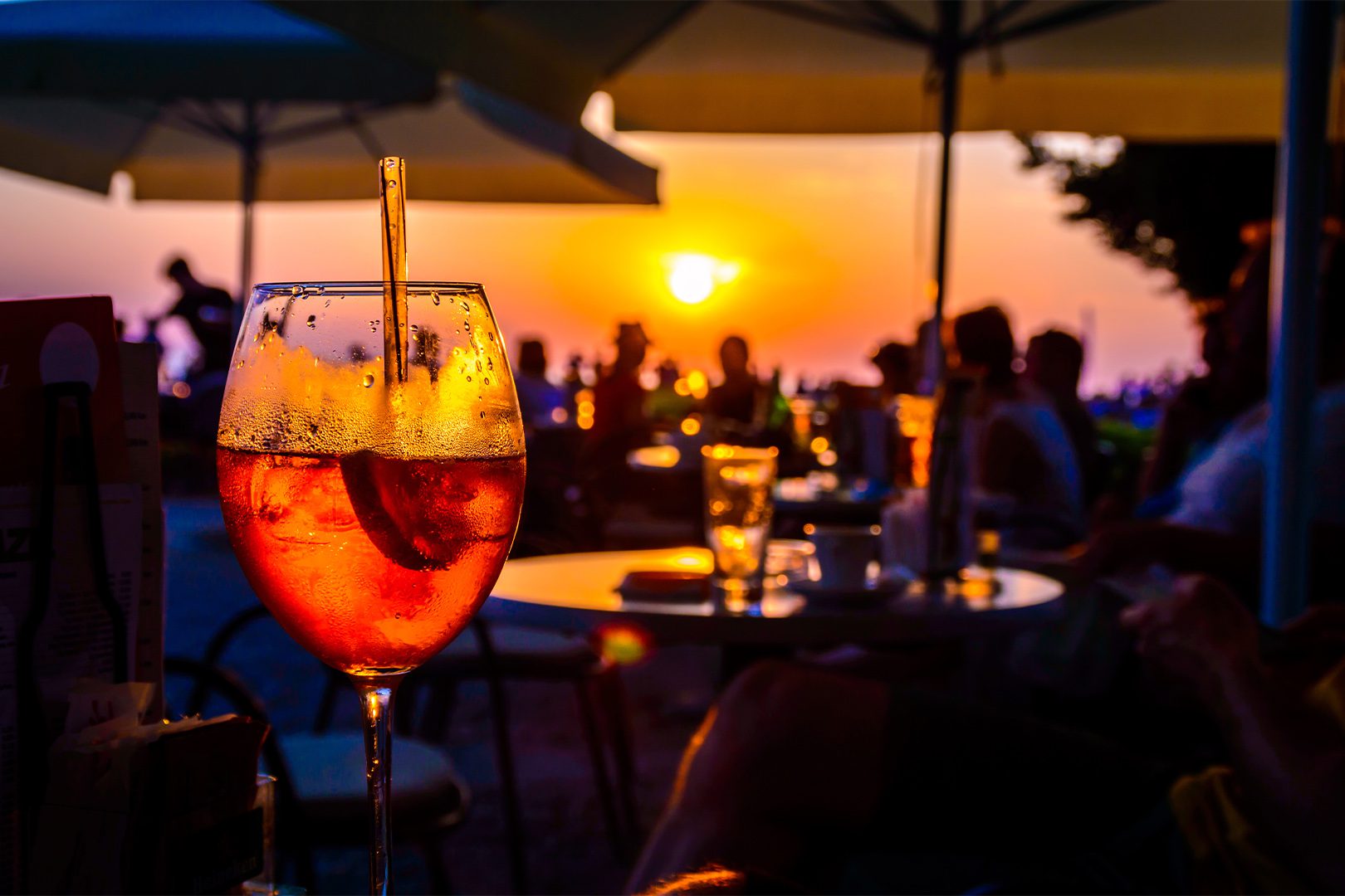 A glass of cold orange cocktail at the sunset on the table of a beach bar